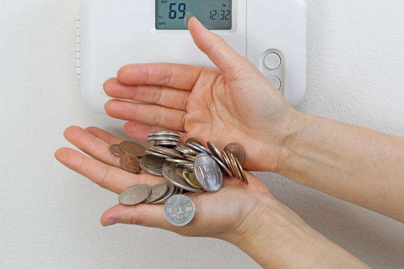 Hands by thermostat with coins falling out.