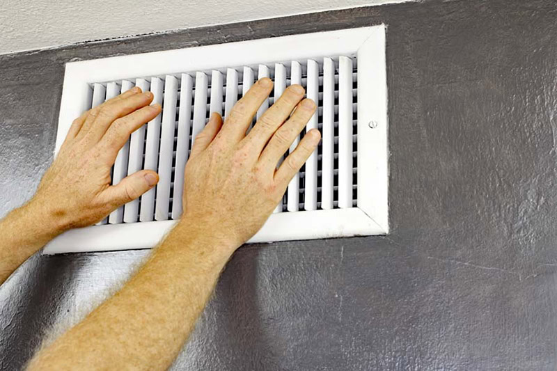 Air-Ton Heating & AC technician feeling air coming out wall vent of Houston, Texas, home.