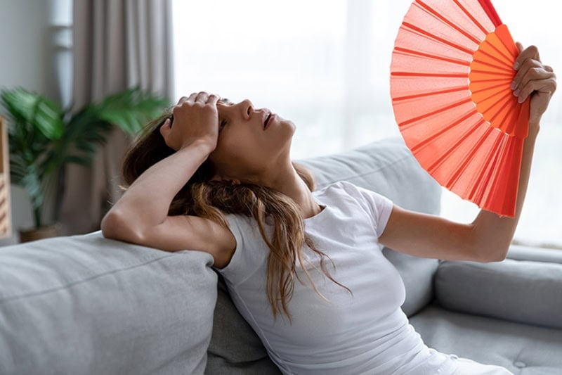 Why Is My AC Blowing Hot Air? Side view exhausted young biracial girl using paper waver.
