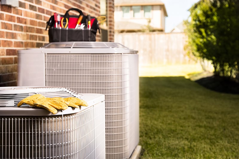 Air-Ton Heating & AC technician toolbag and gloves on top of air conditioning units in West University Place, Texas.