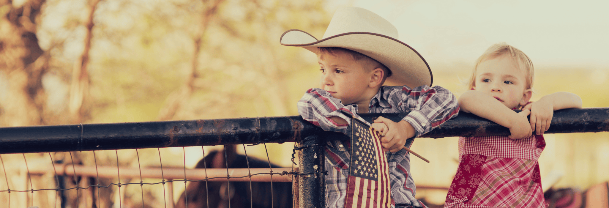 Young cowboy and cowgirl sitting on rail at Houston, Texas, ranch.