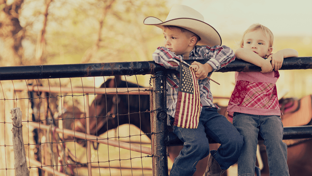 Young cowboy and cowgirl sitting on rail at Houston, Texas, ranch.