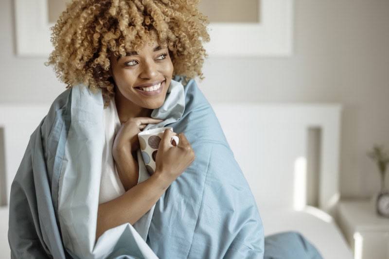 Woman wrapped in blanket enjoying a cup of tea after her furnace maintenance was completed.