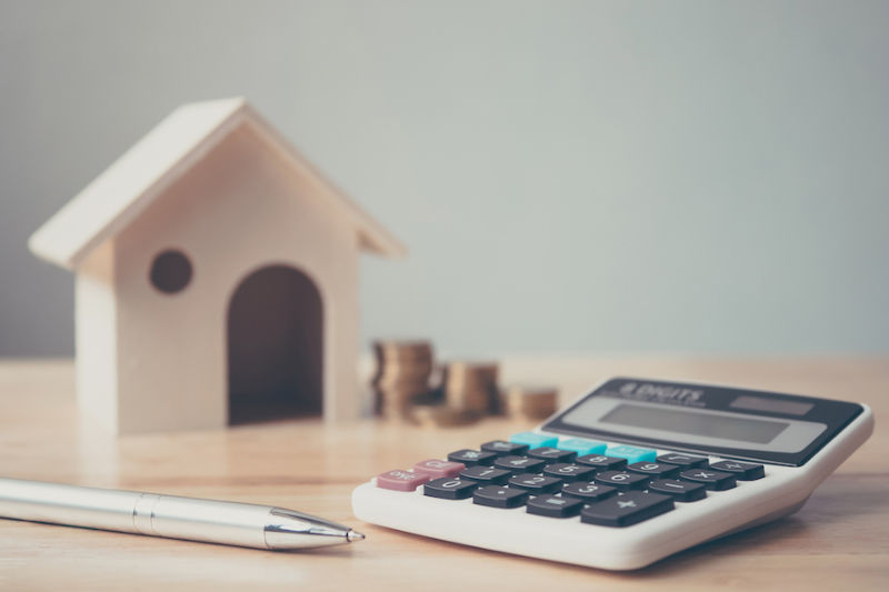 Little house next to coins with calculator and pen.